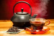 Théière chinoise, posée sur une table à côté d'une tasse de thé fumante et de feuilles de thé séchées