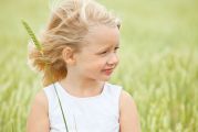 Petite fille blonde dans un champs de blé tenant un épi