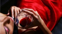 femme en tenue en satin rouge buvant un verre de vinrouge