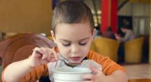 Un enfant mange une soupe dans un bol avec une cuillère dans une cantine