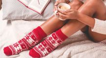 une femme boit une tisane chaude, lit un livre et porte des chaussettes de Noël