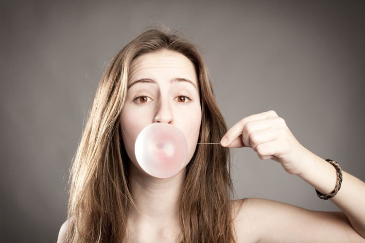 Jeune fille faisant une bulle de chewing-gum et s’apprêtant à l'éclater avec une aiguille 
