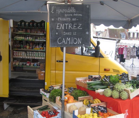 Camionnette jaune de l'épicerie itinérant l'Hirondelle et cagettes de fruits et légumes exposées