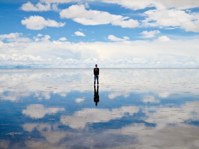 Désert de sable bolivien. Une fine couche d'eau renvoie le reflet d'un homme debout au milieu du paysage