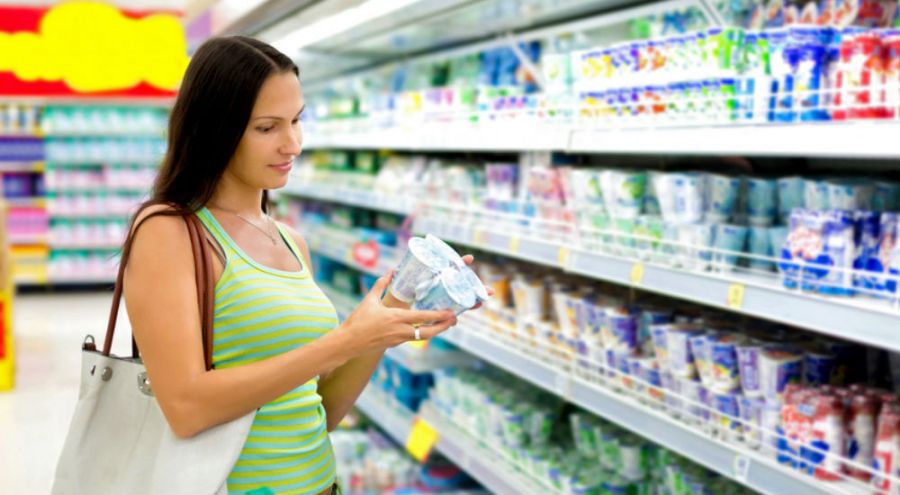 Femme lisant l'étiquette de yaourts dans un rayon de supermarché