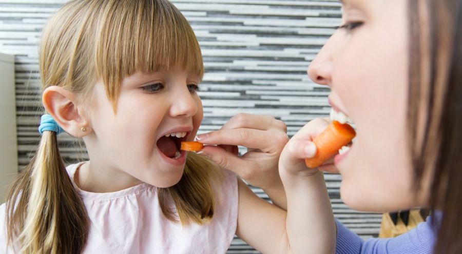 Une petite fille et sa mère se donnent mutuellement à manger une rondelle de carotte