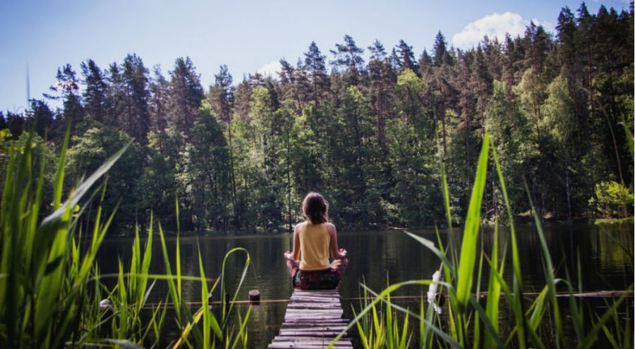 une femme médite sur un pont devant un lac et une forêt