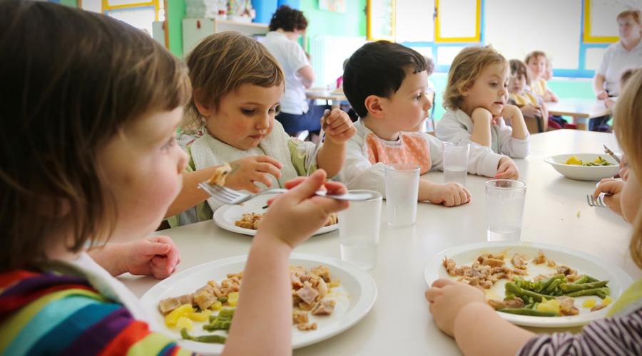Différents enfants mangeant à la table d'une cantine scolaire
